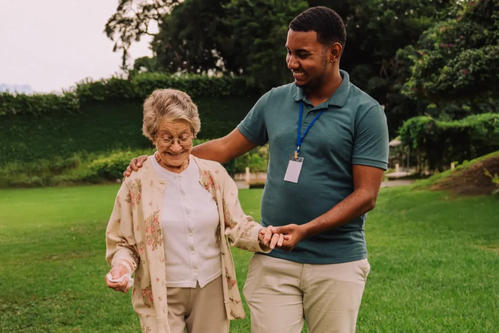Male caregiver walking in garden with elderly woman