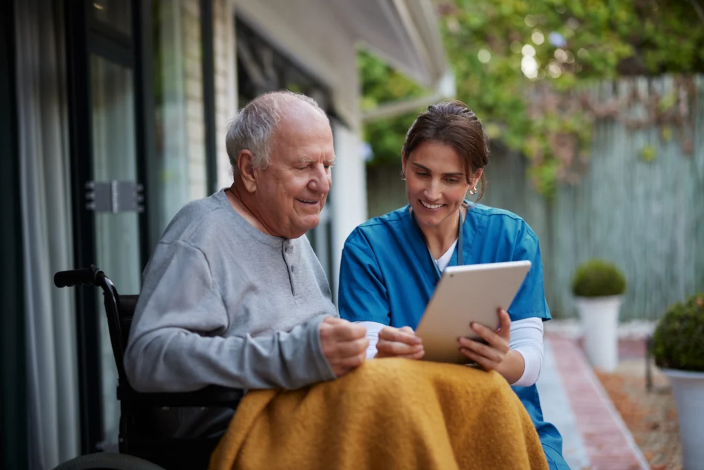 Careful nurse assisting a senior man while using digital tablet on patio.