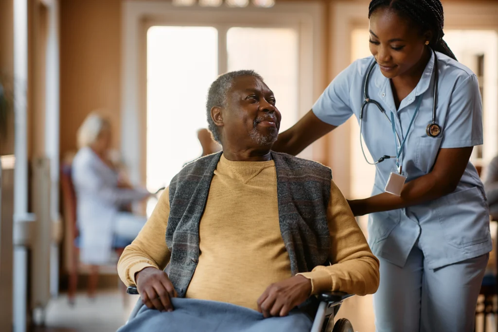 Senior man in wheelchair talking to a nurse at residential care home.